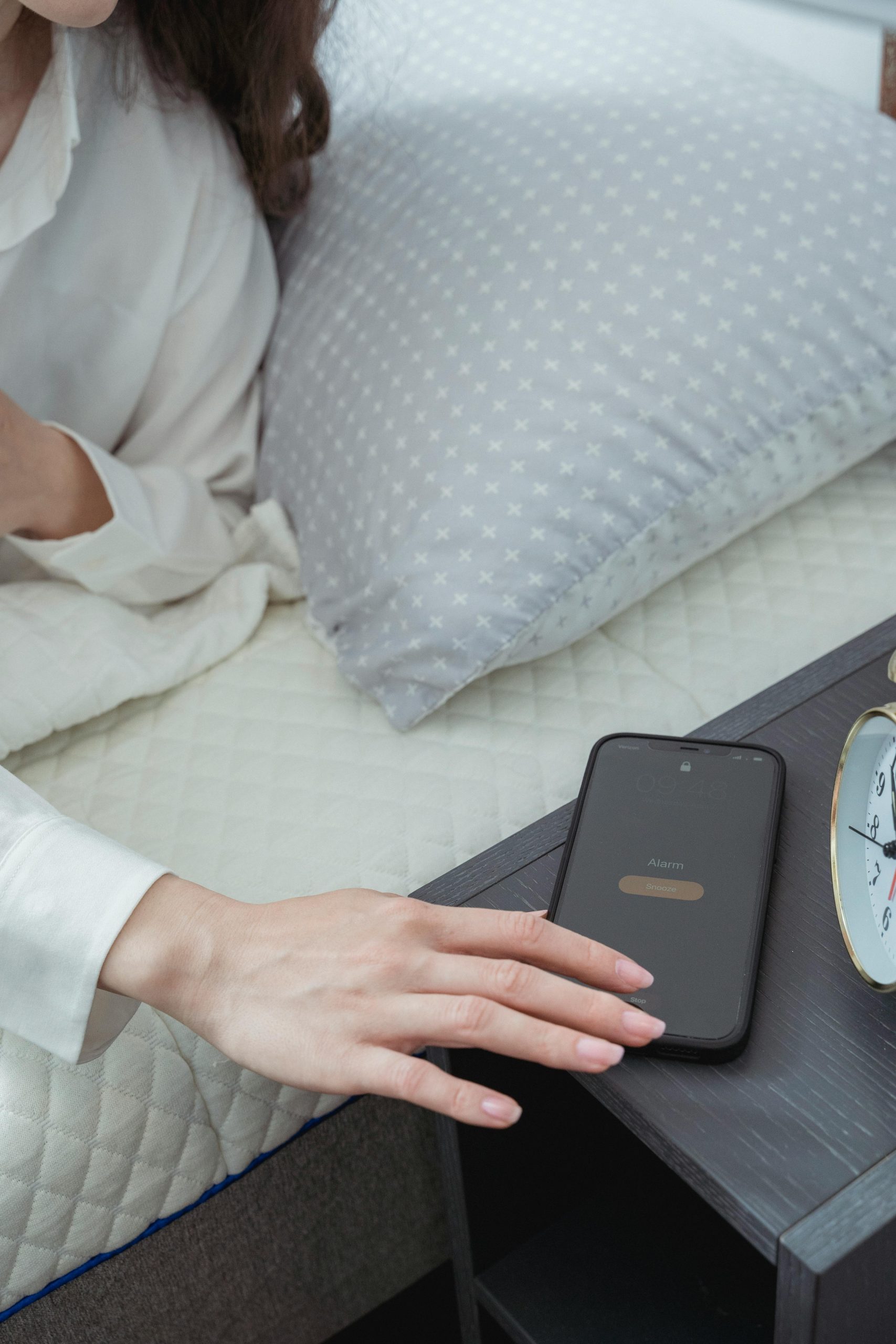 Une personne dans un lit tend la main pour arrêter l'alarme de son smartphone sur une table de chevet.