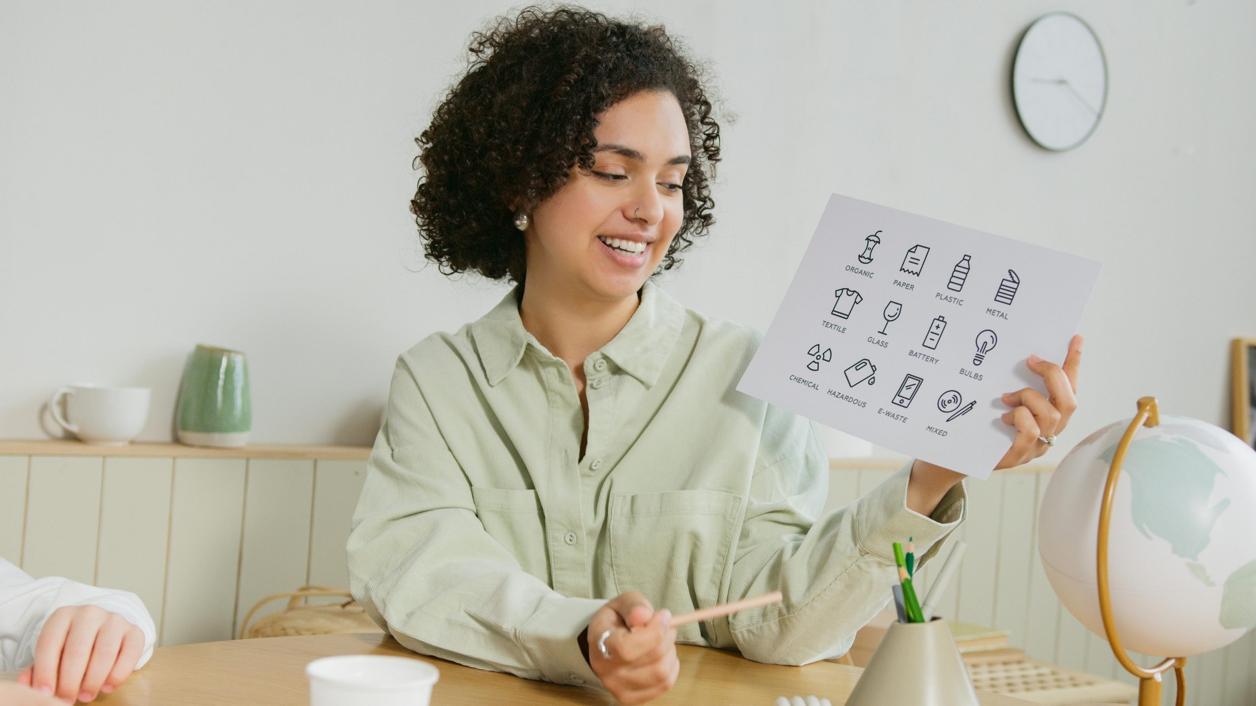Une enseignante joyeuse assise à une table, tenant un tableau éducatif, avec un globe à proximité.