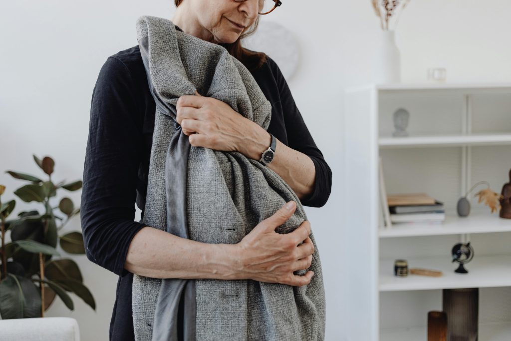 Une femme âgée serrant étroitement un manteau, exprimant des émotions de solitude et de chagrin.
