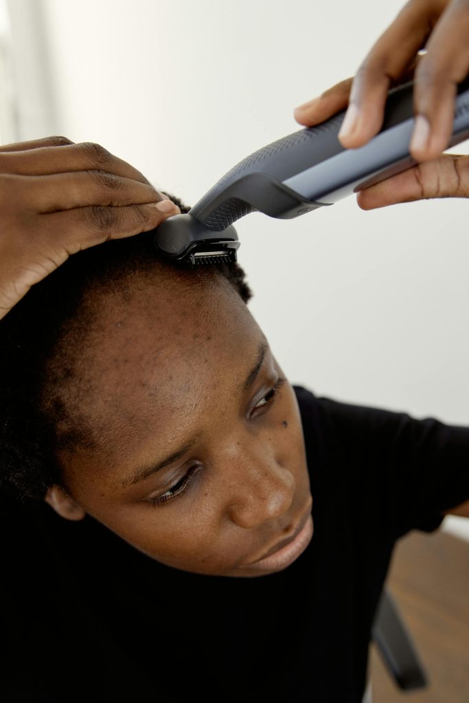 Close-up d'une femme africaine utilisant une tondeuse pour se raser la tête à l'intérieur.
