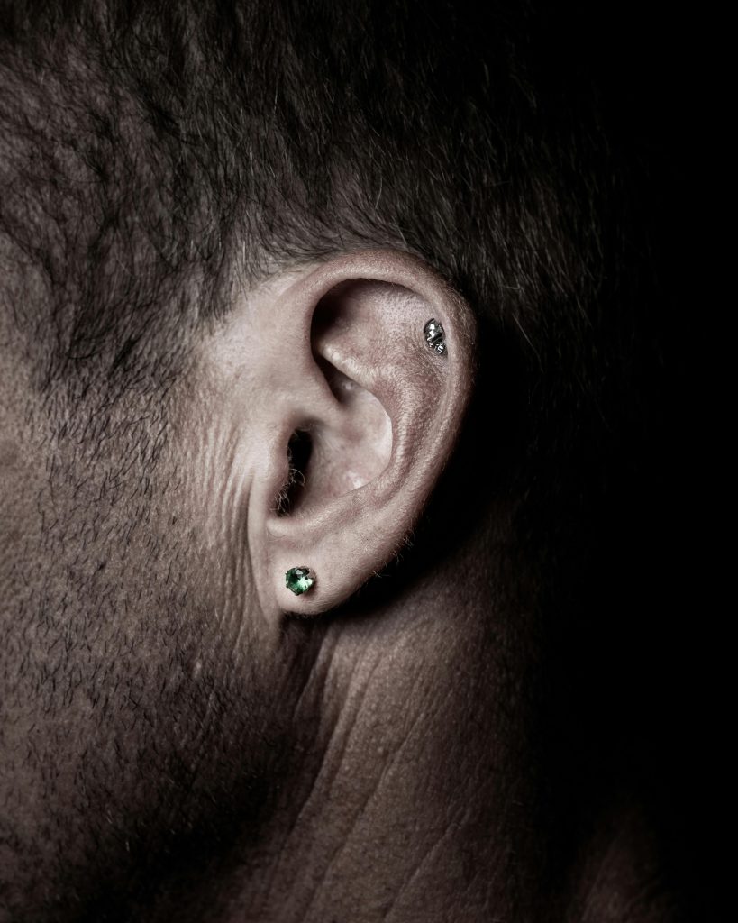 Détail en gros plan d'une oreille humaine avec plusieurs piercings en lumière tamisée.