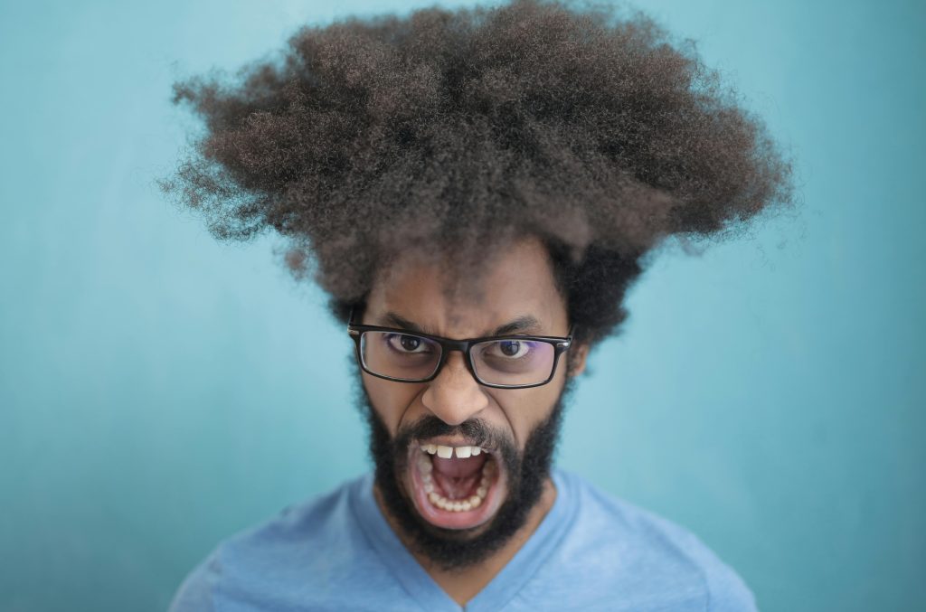 Portrait d'un homme aux cheveux afro portant des lunettes, exprimant une émotion sur fond bleu