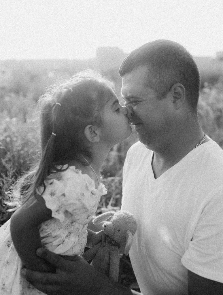 Black and white photo of a loving father and daughter sharing a tender moment outdoors. Photo en noir et blanc d'un père et de sa fille partageant un moment tendre en plein air.