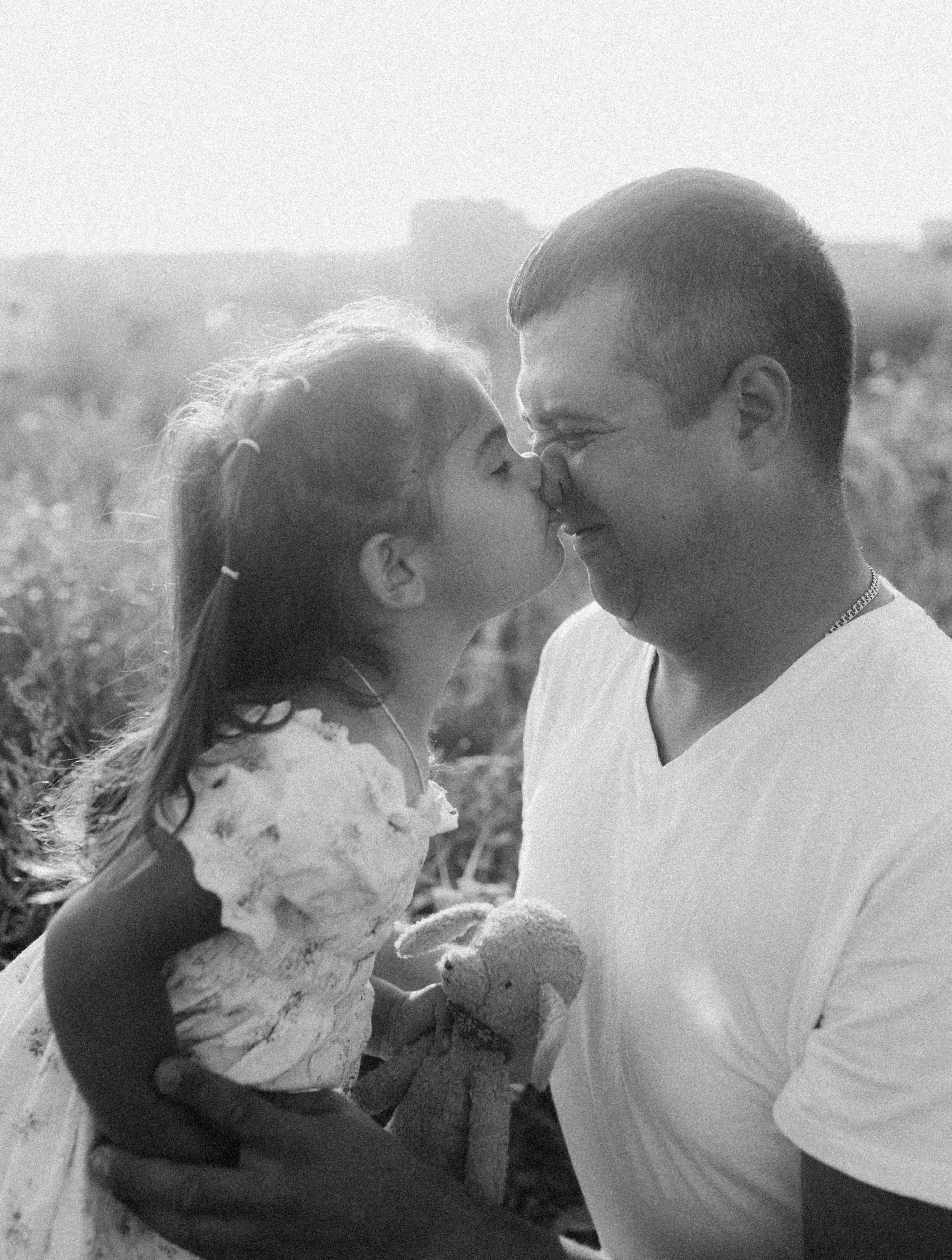 Black and white photo of a loving father and daughter sharing a tender moment outdoors. Photo en noir et blanc d'un père et de sa fille partageant un moment tendre en plein air.