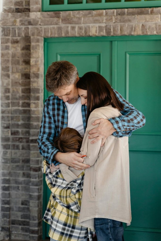 Family of three hugging warmly in front of a green door symbolizing love and unity. Famille de trois personnes s'étreignant chaleureusement devant une porte verte symbolisant l'amour et l'unité.