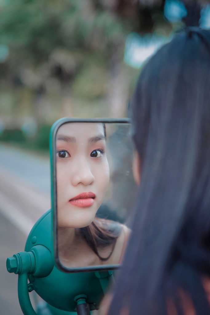 Close-up d'une jeune femme observant son reflet dans un rétroviseur extérieur.