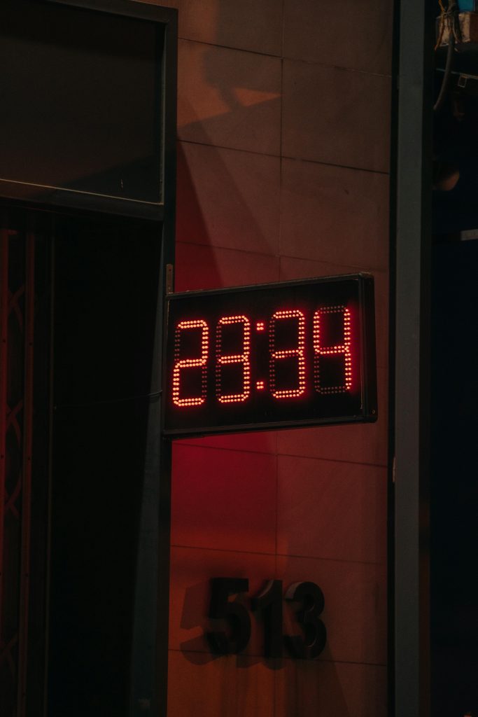 Photo d'une horloge numérique rouge affichant l'heure sur un bâtiment urbain, cadre nocturne.