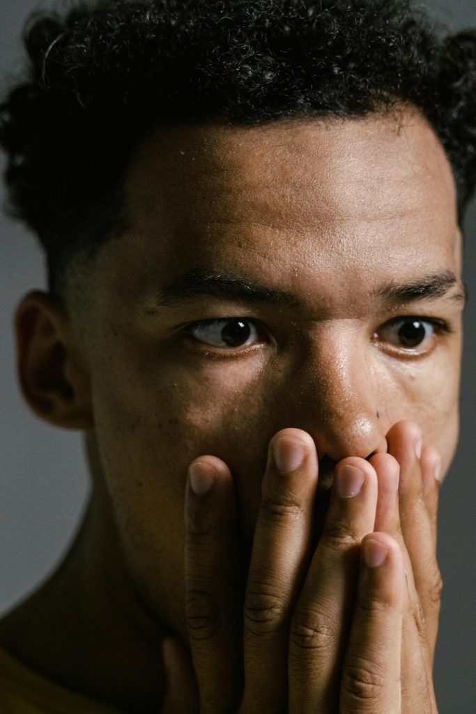 Close-up portrait d'un jeune homme anxieux se couvrant la bouche, indiquant du stress et de l'inquiétude.