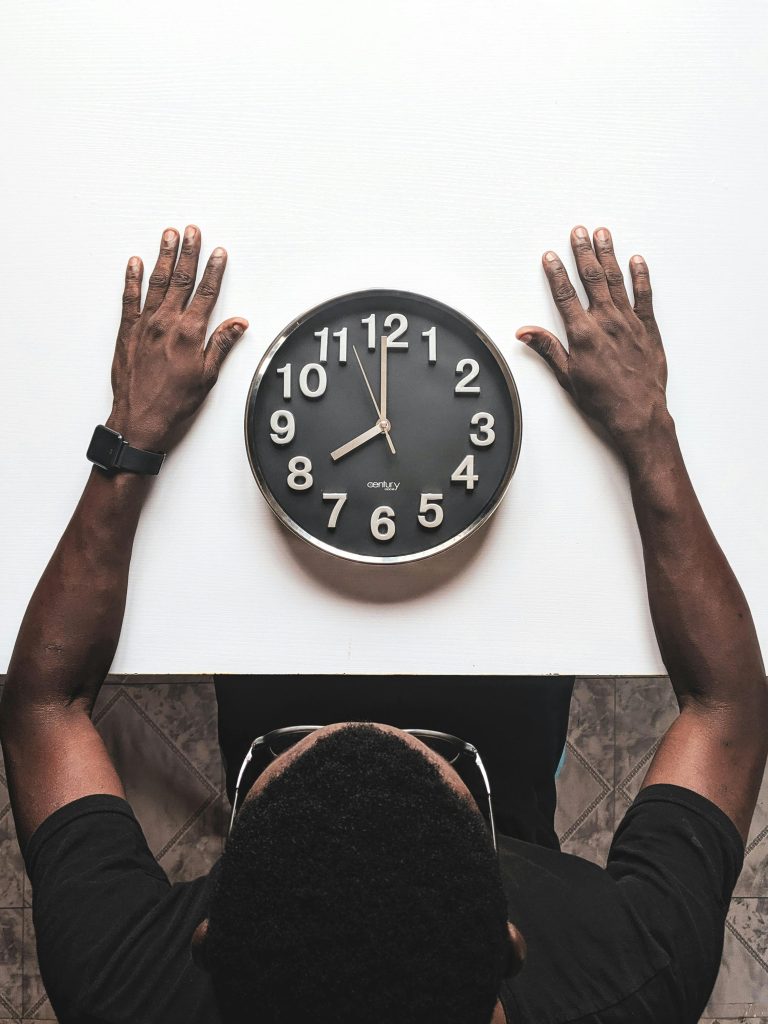 Vue en plongée d'un homme avec une Apple Watch observant une horloge sur une table blanche.