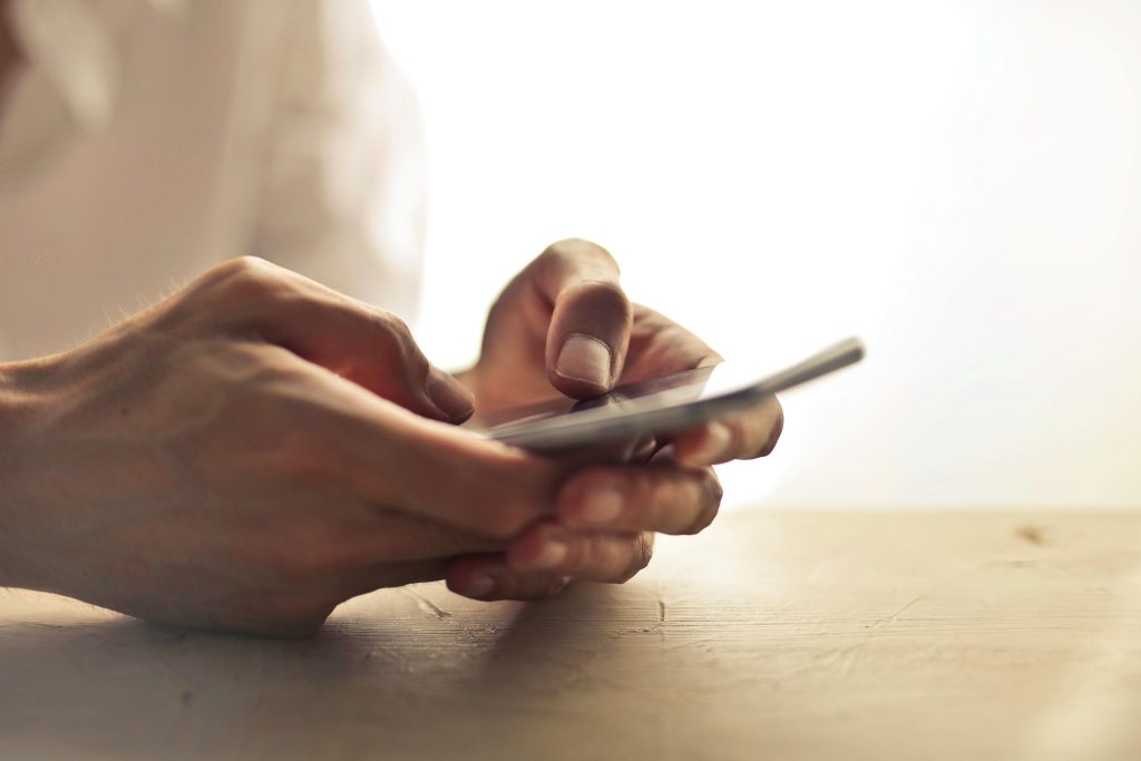 Gros plan des mains d'une personne tenant un smartphone sur une table à l'intérieur.