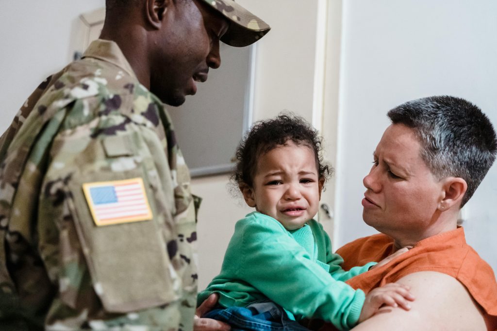 A family reunion depicting a soldier, mother, and crying child, showcasing strong emotions. Une réunion de famille représentant un soldat, une mère et un enfant en pleurs, illustrant des émotions fortes.
