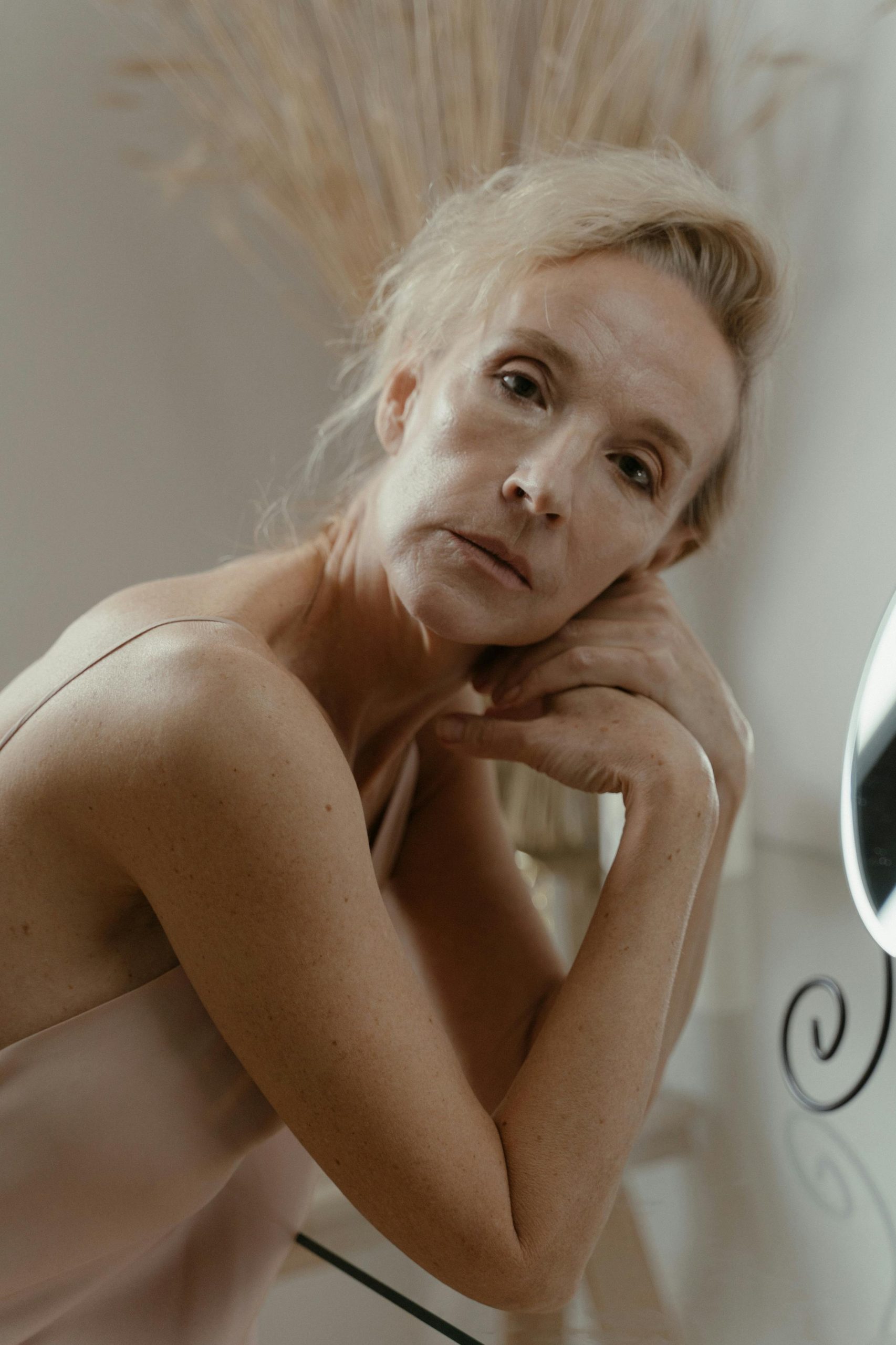 Portrait réfléchi d'une femme âgée assise devant une surface en verre réfléchissante à l'intérieur.