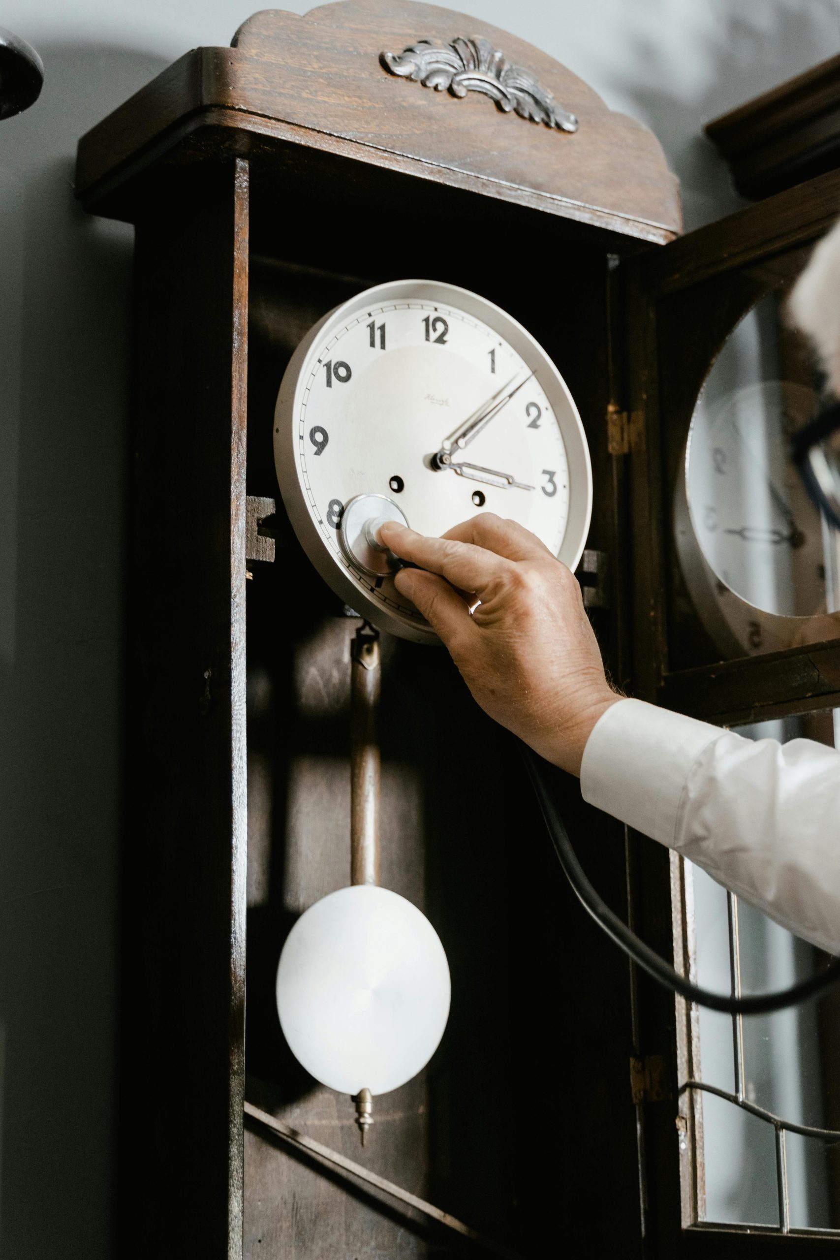 Close-up of a hand adjusting a vintage wall clock mechanism with a stethoscope. Gros plan d'une main ajustant un mécanisme de pendule vintage avec un stéthoscope.