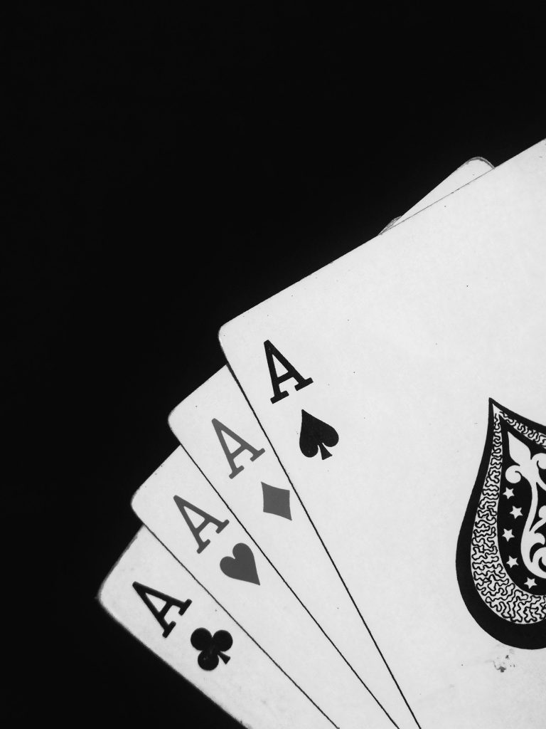 A dramatic black and white image showcasing four aces in a card game, set against a black background. Une image dramatique en noir et blanc mettant en avant quatre as dans un jeu de cartes, sur fond noir.