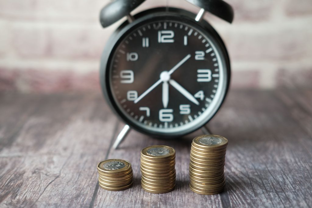 Stacked coins and a classic alarm clock symbolize the value of time and money. Des pièces empilées et une horloge classique symbolisent la valeur du temps et de l'argent.