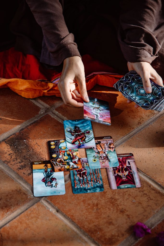 A close-up view of hands engaged in a tarot card reading on a tiled floor, creating a mystical atmosphere. Une vue rapprochée de mains engagées dans une lecture de tarot sur un sol carrelé, créant une atmosphère mystique.