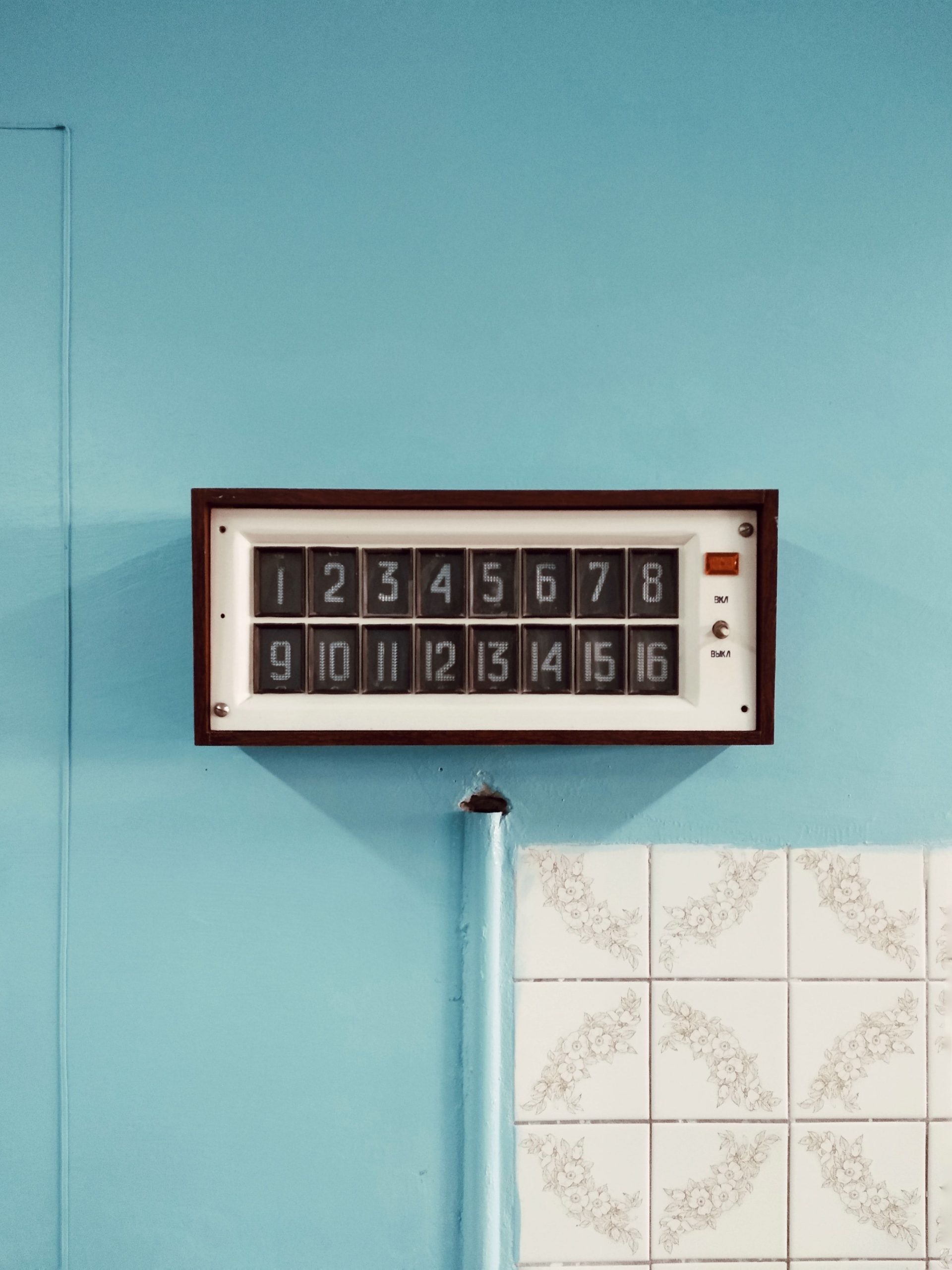 Retro wall clock displaying numbers on a blue tiled backdrop, perfect for decor inspiration. Horloge murale rétro affichant des chiffres sur un fond de carrelage bleu, parfaite pour l'inspiration en matière de décoration.
