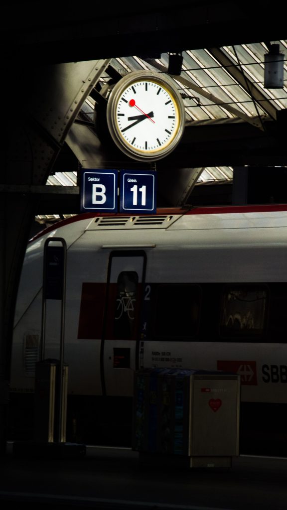 Nighttime view of Zürich railway station platform, featuring a clock and SBB train with seating information. --- Vue nocturne du quai de la gare de Zürich, présentant une horloge et un train SBB avec informations de places assises.