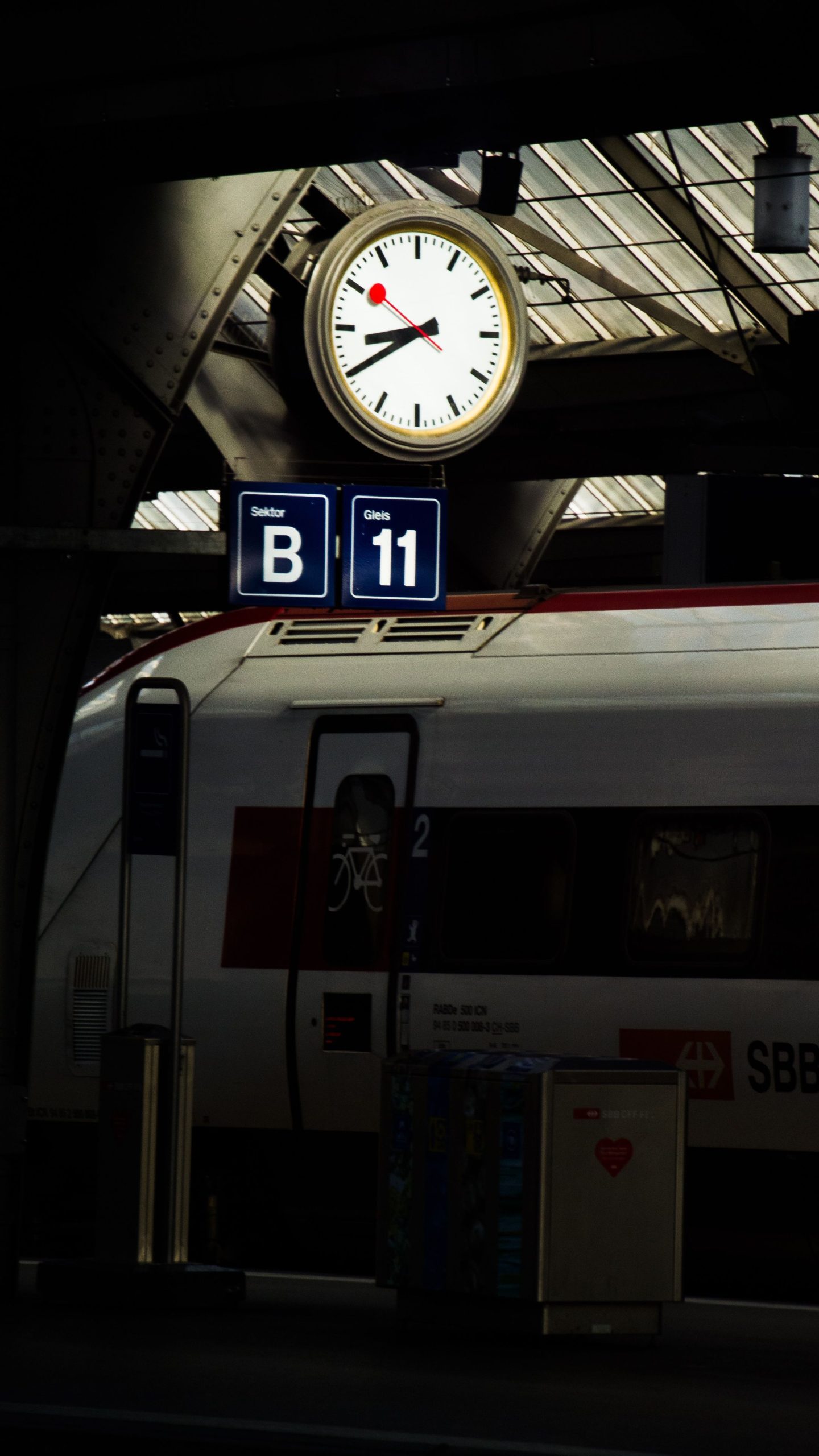 Nighttime view of Zürich railway station platform, featuring a clock and SBB train with seating information. --- Vue nocturne du quai de la gare de Zürich, présentant une horloge et un train SBB avec informations de places assises.