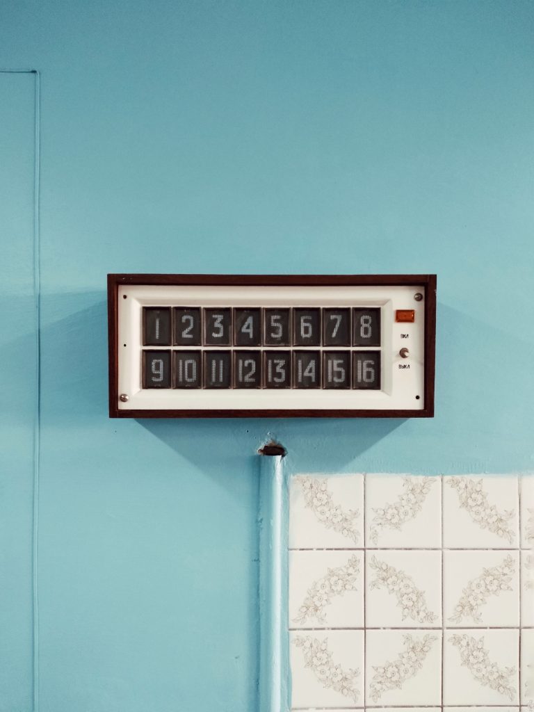 Retro wall clock displaying numbers on a blue tiled backdrop, perfect for decor inspiration. Horloge murale rétro affichant des chiffres sur un fond de carreaux bleus, parfaite pour l'inspiration en matière de décoration.