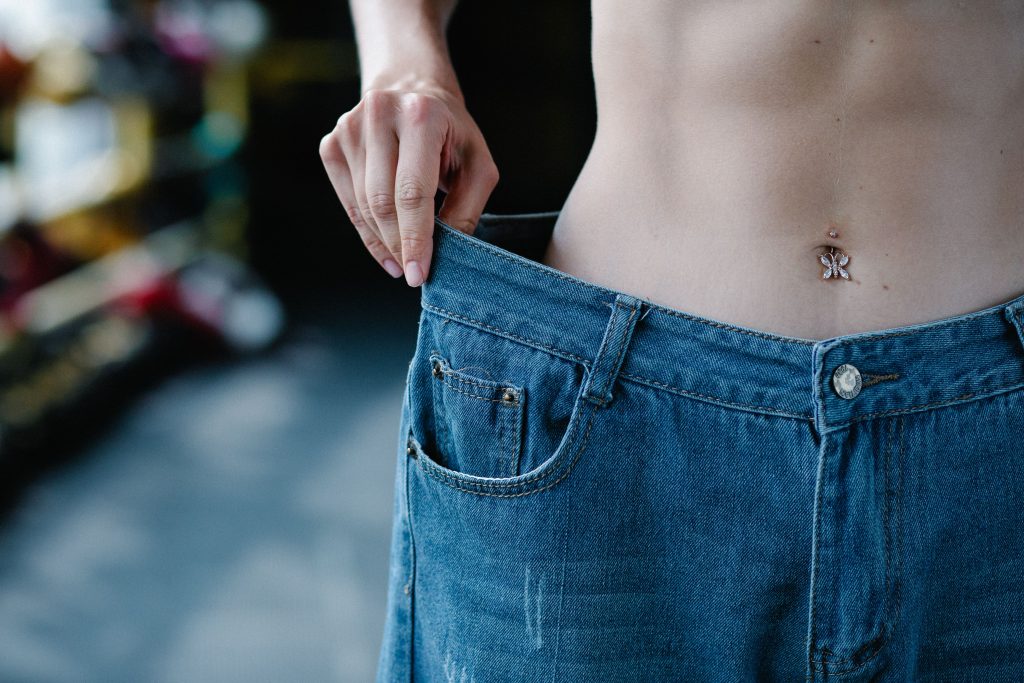 Close-up view of a slim waist and loose jeans representing weight loss or fitness progress. Vue rapprochée d'une taille fine et d'un jean ample représentant une perte de poids ou des progrès en matière de remise en forme.