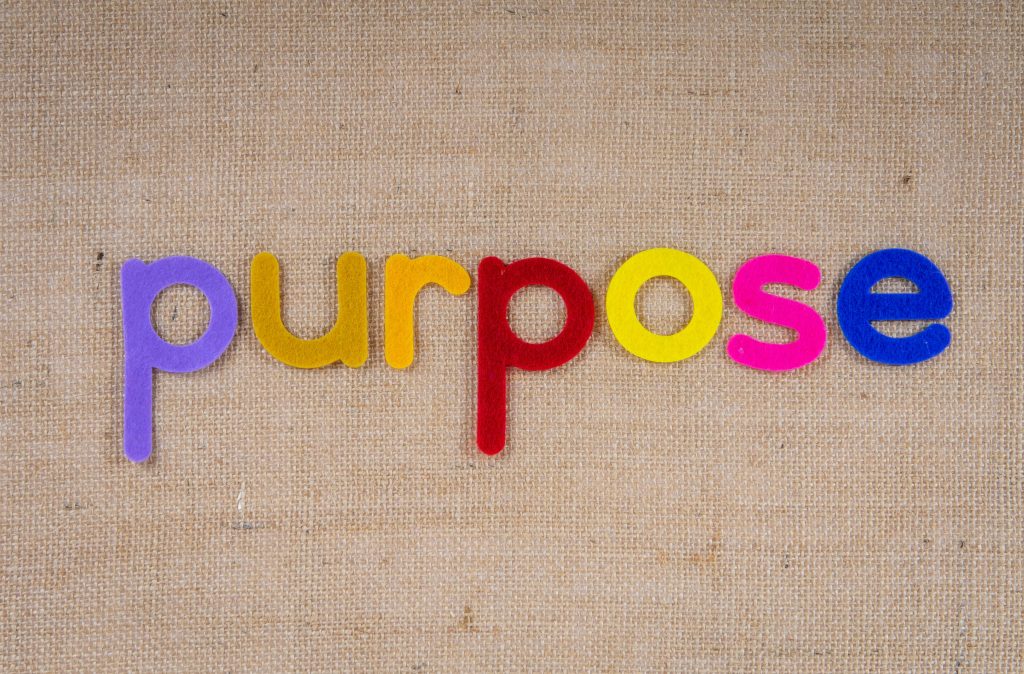 Colorful felt letters spelling 'purpose' on a textured fabric background with ample copyspace. Des lettres en feutre colorées épelant « purpose » sur un fond de tissu texturé avec beaucoup d'espace pour le texte.