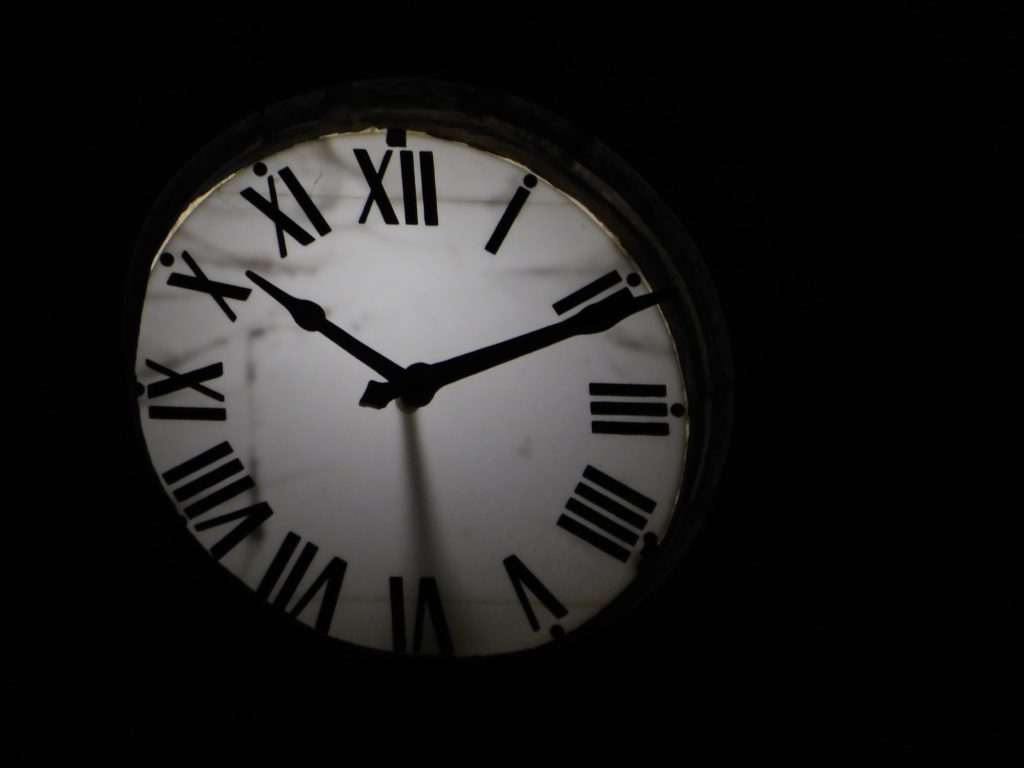 Round mechanical clock with black arrows and numbers on white face ticking on black background in darkness Horloge mécanique ronde avec des aiguilles noires et des chiffres sur un cadran blanc tiquetant sur fond noir dans l'obscurité