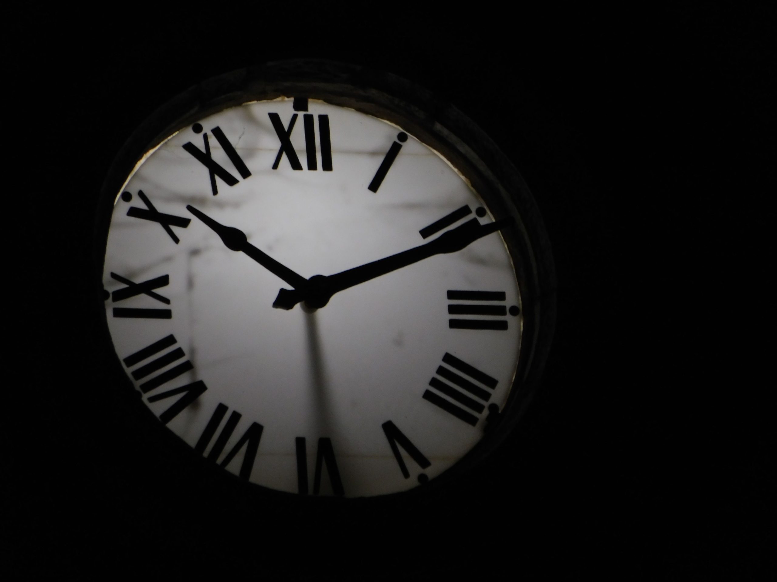 Round mechanical clock with black arrows and numbers on white face ticking on black background in darkness Horloge mécanique ronde avec des aiguilles noires et des chiffres sur un cadran blanc tiquetant sur fond noir dans l'obscurité