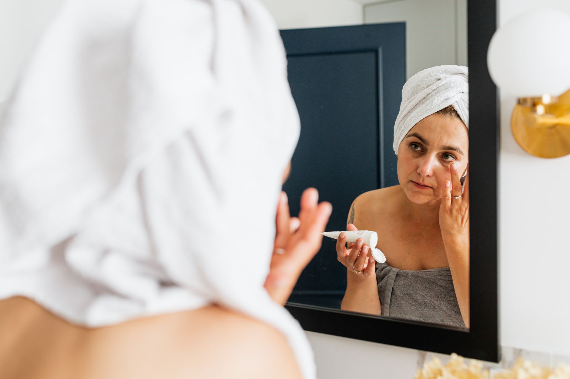 Femme appliquant une crème hydratante devant un miroir